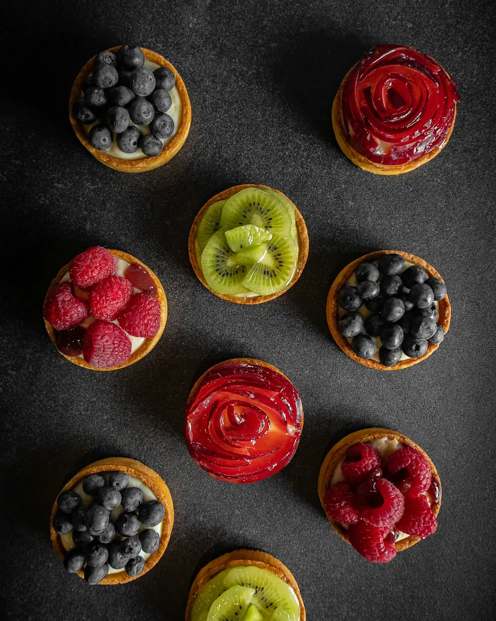 Fruit tartlets with berries and kiwi on black slate
