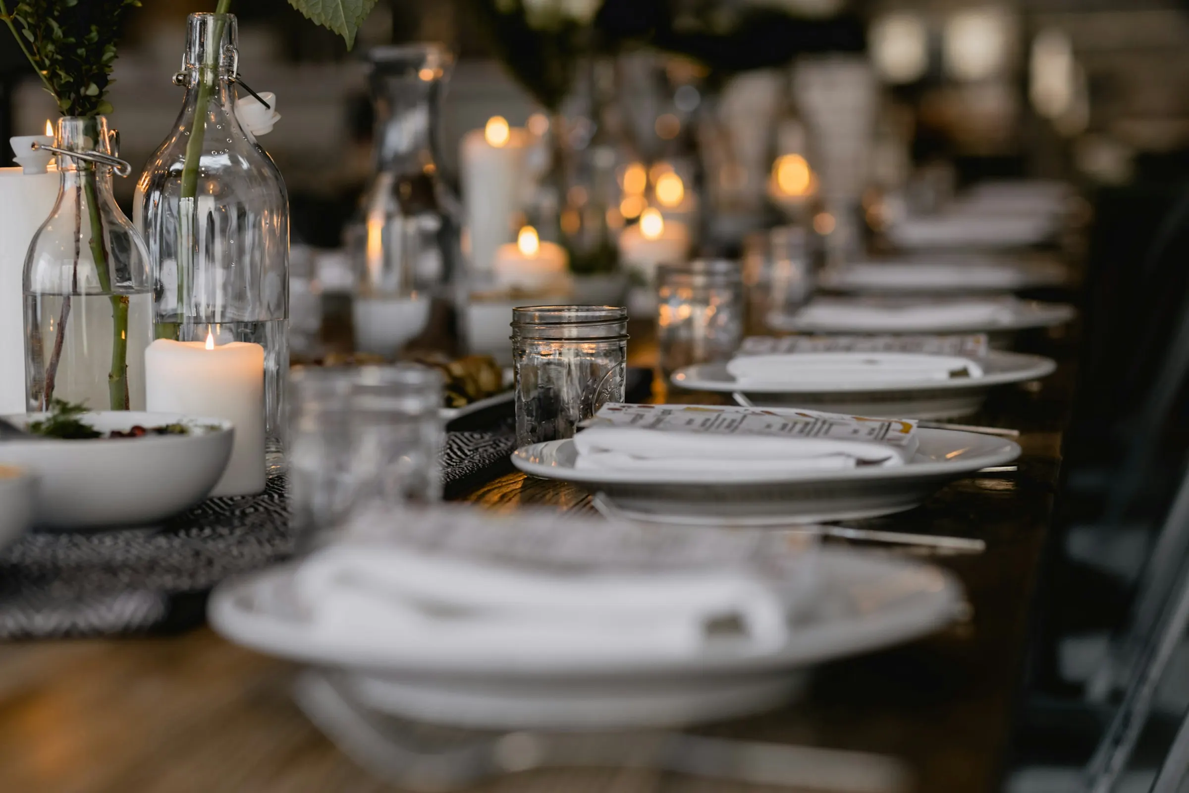 A long dinner table set with white plates and glowing candles
