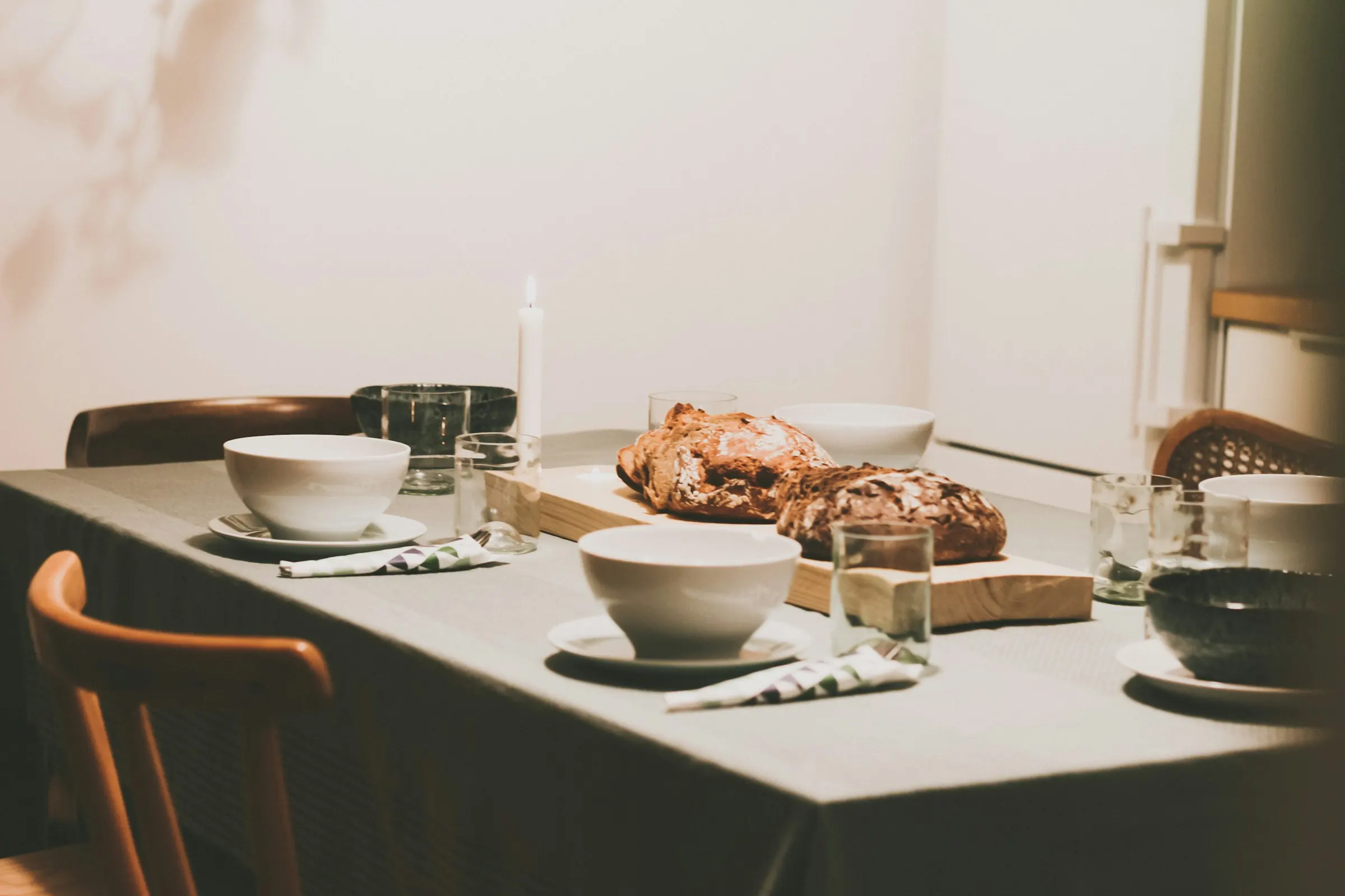 A long table set with linen, stoneware bowls, and a shared meal in soft daylight