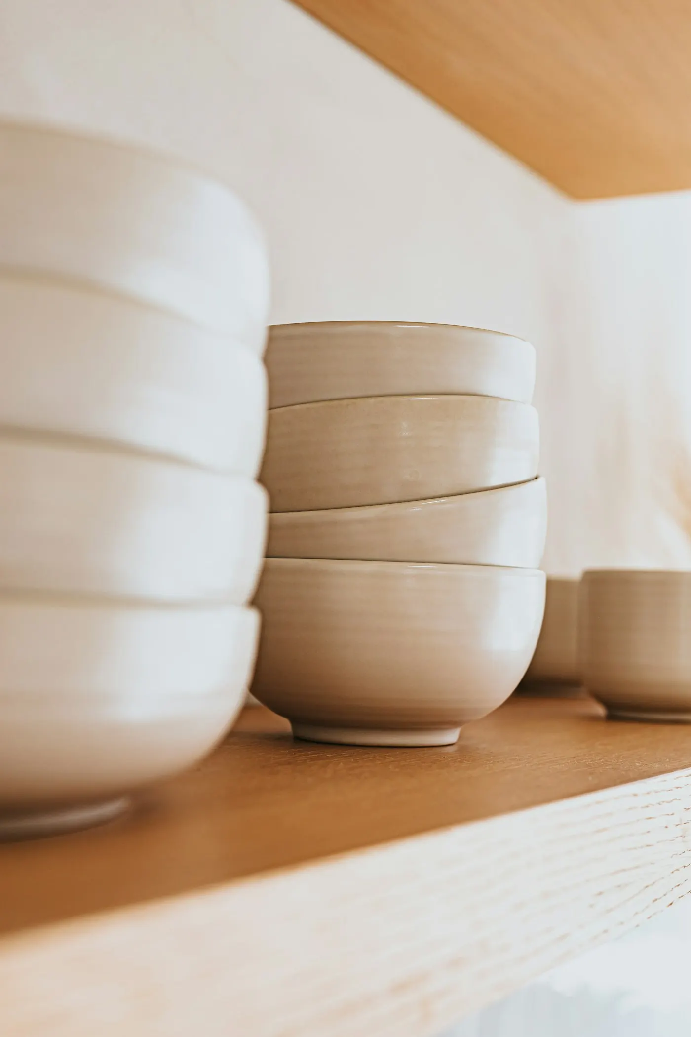 Stacked cream stoneware bowls on a wooden shelf
